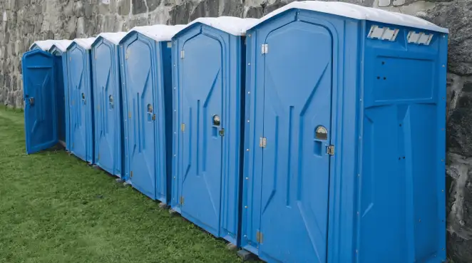 Row of blue portable toilets lined up on grass against a stone wall for event sanitation in Ogden, UT