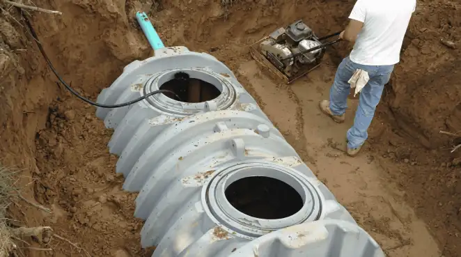 Septic tank installation showing a technician compacting soil around a new poly septic tank in an excavation pit in Ogden, UT